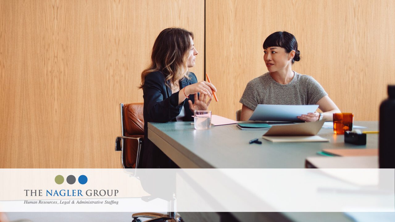 two professional women sit together at an office meeting room table discussing business